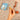 Hand holding a dog treat with a blue pet toy box and orange rope toy in the background on a carpeted floor.